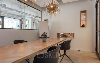 Modern office space at Roggestraat 111, Apeldoorn, featuring contemporary lighting and a wooden table with chairs, ideal for small meetings.