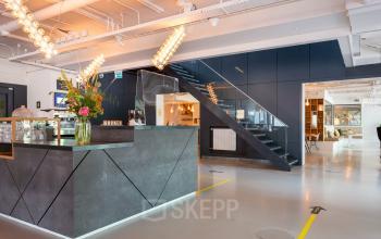 Modern, well-lit interior space at Roggestraat 111, Apeldoorn with sleek reception desk, glass stairway, and contemporary lighting, perfect for office space rental.