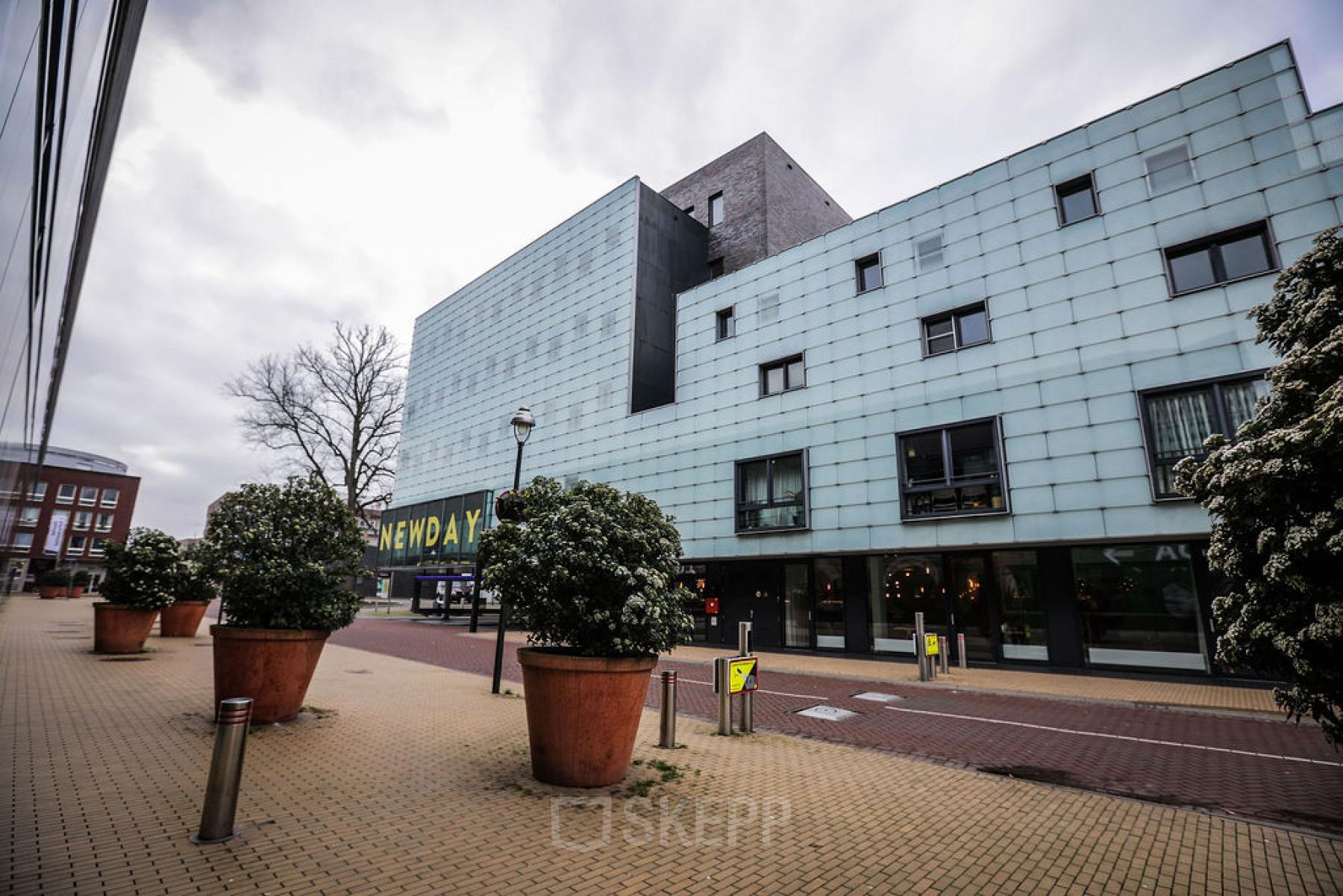 Modern office building located at Roggestraat 111, Apeldoorn with a contemporary facade, large windows, and potted plants lining the walkway, perfect for office space rental.