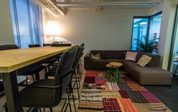 Cozy and vibrant office space at Jansbuitensingel 7, Arnhem Centrum, perfect for rent with a mix of seating options, colorful rug, and warm lighting.
