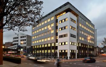 Exterior view of the office building located at Vossenstraat 6, Arnhem Centrum, Arnhem. A multi-story building with illuminated windows visible from the street. Ideal for office space rental.
