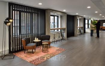 Office interior at Vossenstraat 6, Arnhem Centrum, Arnhem with modern furnishings, tall windows, and several individuals engaged in conversation. Ideal office space rental opportunity.