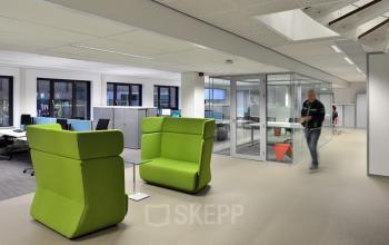 Modern office space rental at Vossenstraat 6, Arnhem Centrum, featuring green lounge chairs, workstations, and a glass-walled meeting room.