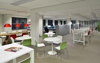 Modern office at Vossenstraat 6, Arnhem Centrum with collaborative workspaces, and seating areas. Bright lighting and contemporary furniture are present.