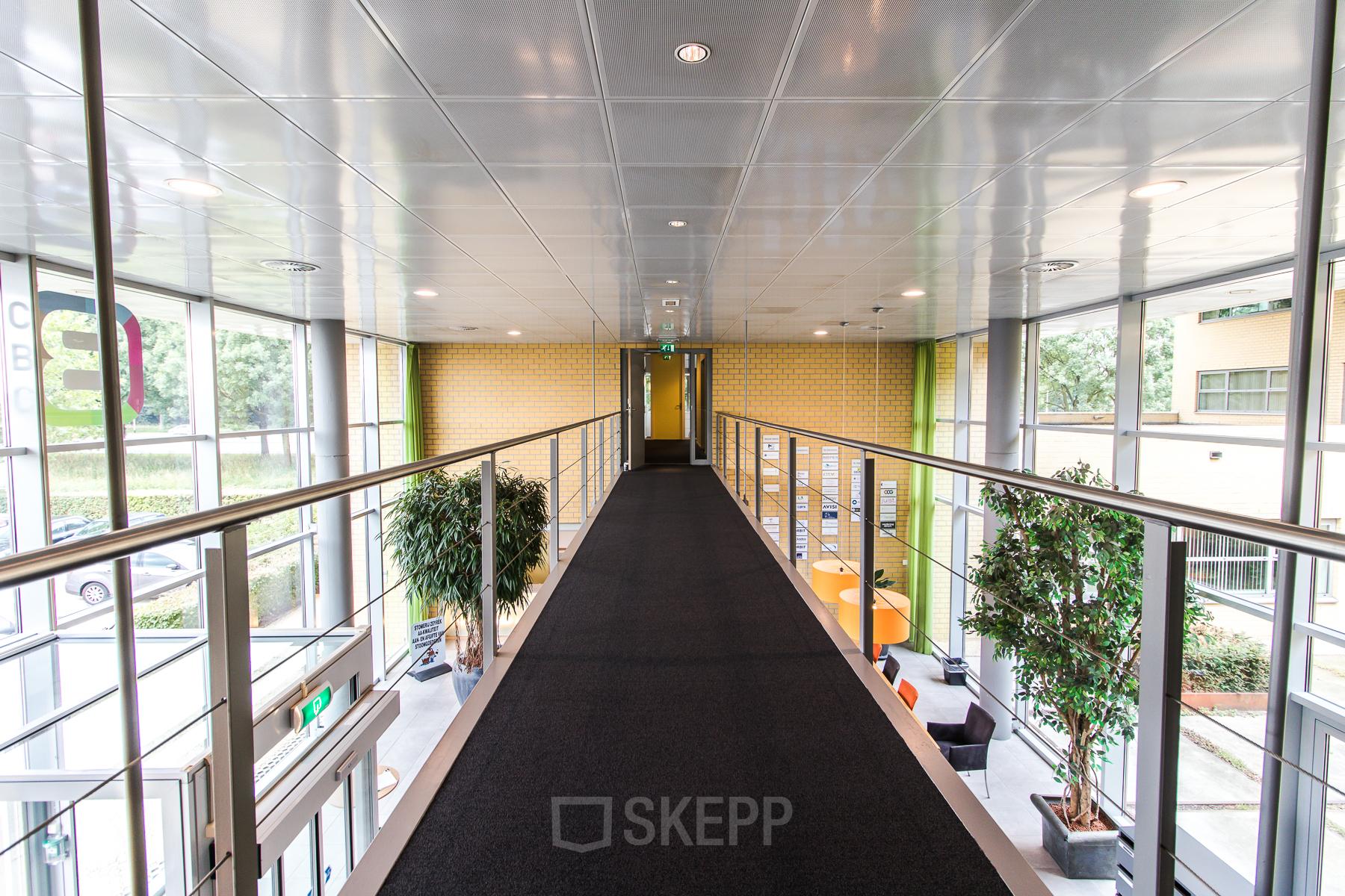 Spacious and well-lit corridor in Meander 251 office space rental in Arnhem IJsseloord, featuring modern furnishings and green plants.