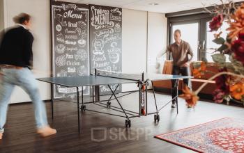Two people engage in a friendly game of ping pong in a casual office space at Vlamoven 34, Arnhem IJsseloord, ideal for rent office space seekers.