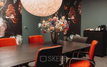 Office space rental at Vlamoven 34, Arnhem IJsseloord featuring a meeting room with a dark wooden table, vibrant red chairs, and decorative floral arrangements.