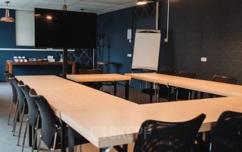 Conference room at Vlamoven 34, Arnhem IJsseloord, ideal for office space rental, featuring modern furnishings with U-shaped tables and a large screen.