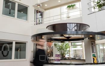 Modern office to rent at Vlamoven 34, Arnhem IJsseloord, featuring an open atrium with individuals walking through the reception area.