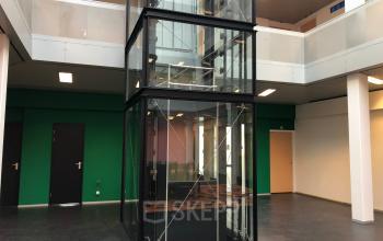 Interior view of an office building at Simon Stevinweg 27, Arnhem Oost, featuring a glass elevator and modern entryway.