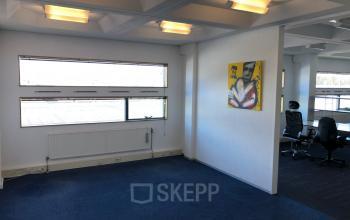 Bright office space rental at Simon Stevinweg 27, Arnhem Oost, featuring fluorescent lighting, blue carpet, white walls, and modern artwork.