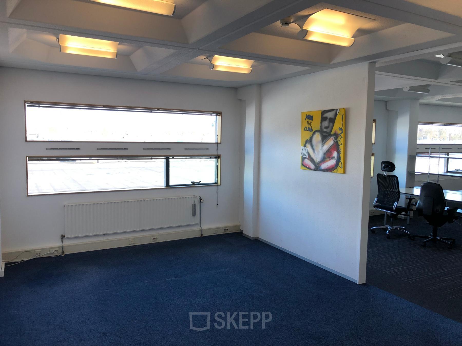 Bright office space rental at Simon Stevinweg 27, Arnhem Oost, featuring fluorescent lighting, blue carpet, white walls, and modern artwork.