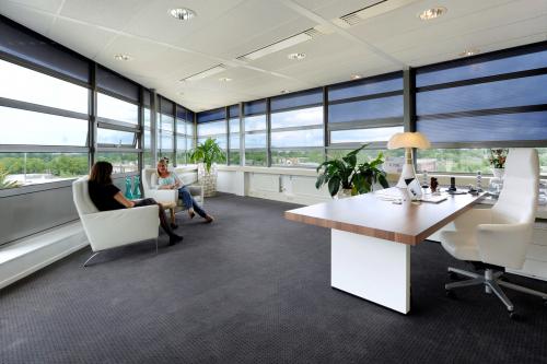 Modern office to rent at Mr D.U. Stikkerstraat 10, Arnhem Zuid, with large windows, contemporary furniture, and business professionals having a meeting.
