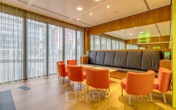 Cozy lounge area available for office space rental at Meester D.U. Stikkerstraat 11 in Arnhem Zuid, Arnhem; features comfortable orange chairs and a long bench with modern decor.