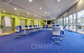 Spacious, well-lit office space rental at Meester D.U. Stikkerstraat 11, Arnhem Zuid, Arnhem featuring blue carpet, modern chairs, large tables, and a whiteboard.
