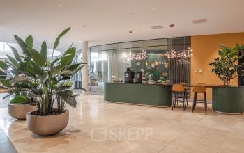 Modern reception area in office building at Rijksweg-West 2, Arnhem Zuid, Arnhem with green reception desk, barstools, indoor plants, and contemporary lighting.