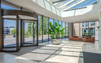 Bright, spacious entrance lobby at Rijksweg-West 2, Arnhem Zuid, featuring a revolving door, skylights, modern seating, and large potted plants.