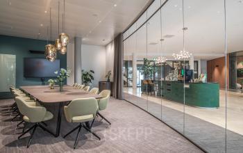 Modern conference room at Rijksweg-West 2, Arnhem Zuid, Arnhem, featuring a large table, chairs, and glass walls with a view into a green-themed reception area.