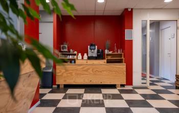 Bright lounge area at Overcingellaan 17, Assen featuring a wooden counter with a coffee machine, contrasting red walls, and checkered flooring. Ideal for office space rental.