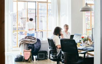 Cozy Barcelona office space with people working at desks and interacting, featuring large windows allowing natural light.