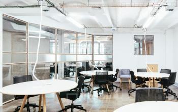 Bright office space with several circular tables and black chairs, suitable for collaborative work. Glass partitions add modernity, ideal for office space rental activities.