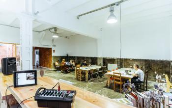Office to rent in Barcelona Gràcia at Carrer de Vilafranca 7, featuring a spacious area with tables and individuals engaged in work activities.
