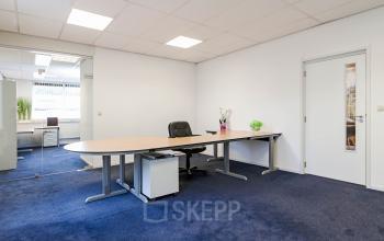 Office space for rent at Poortweg 1, Bergen op Zoom, featuring blue carpet, a large desk with a chair, and glass partitions.