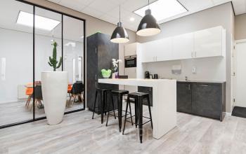 Modern office pantry located at Poortweg 1, Bergen op Zoom with sleek countertops, a high table with bar stools, and a view into a well-lit meeting room.