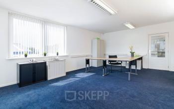 Office space at Poortweg 1, Bergen op Zoom, featuring a bright room with blue carpet, large windows, a desk with a chair, and minimal furnishings.