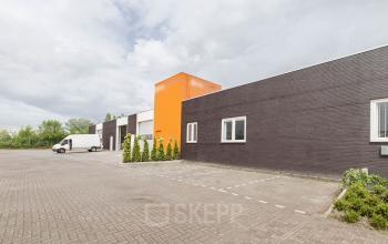 Exterior view of office building at Poortweg 1, Bergen op Zoom, featuring a parking area and a bright orange accent wall.