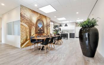 Modern office space with a large table and chairs, stylish decor, and a small kitchenette located at Poortweg 1, Bergen op Zoom, available for office space rental.