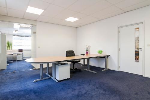 Office space for rent at Poortweg 1, Bergen op Zoom, featuring blue carpet, a large desk with a chair, and glass partitions.