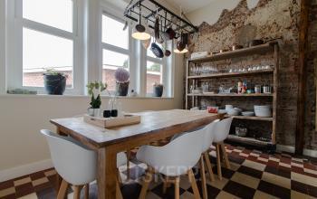 Charming office space rental at Prins Bernhardlaan 64, Bergen op Zoom, featuring a rustic dining area with a wooden table, white chairs, and exposed brick wall.