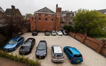 Parking lot with several cars located at Prins Bernhardlaan 64, Bergen op Zoom, adjacent to a brick building.