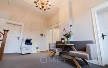 Interior view of an office at Prins Bernhardlaan 64, Bergen op Zoom, featuring a seating area with a small table and a printer in the corner.