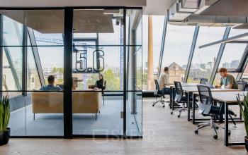 Modernes Büro in der Köpenicker Straße 40-41, Berlin Friedrichshain, mit großen Fenstern, Schreibtischen und Besprechungsraum. Drei Personen arbeiten konzentriert.