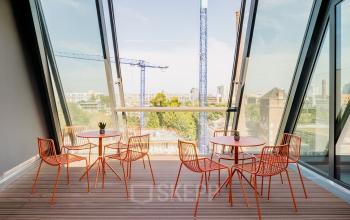 Moderner Büroraum in der Köpenicker Straße 40-41, Berlin Friedrichshain mit Panoramafenstern, Holzlattenboden und minimalistischen orangen Stühlen.