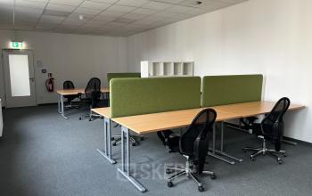 Schlichtes, möbliertes Büro in der Rigaer Straße 71a, Berlin Friedrichshain. Perfekt, um flexibel Büroraum zu mieten. Moderne Arbeitsplätze mit grünen Trennwänden und schwarzen Bürostühlen.