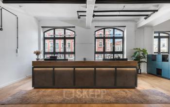 Empfangsbereich im Büro in Edisonstraße 63, Berlin Köpenick. Große Fenster, Holzboden, moderne Empfangstheke und Pflanzen.