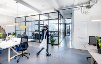 Modernes Büro in Berlin Kreuzberg mit offenen Arbeitsbereichen, Schreibtischen und Glaswänden. Personen arbeiten oder bewegen sich durch den Raum.