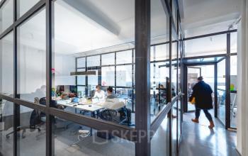 Büroraum mit Glaswänden in der Rudi-Dutschke-Straße 23, Berlin-Kreuzberg, mit arbeitenden Personen an Schreibtischen. Moderne und helle Arbeitsumgebung für Bürofläche mieten.