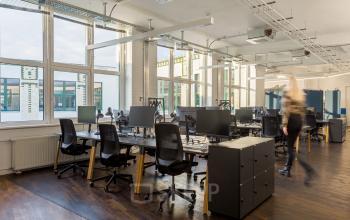 Großer, heller Büroraum im Bürogebäude von Mehringdamm 33 in Berlin-Kreuzberg mit vielen Arbeitsplätzen und modernen Möbeln. Eine Person geht durch den Raum.