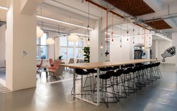 Modernes Büro zur Miete in Berlin Kreuzberg, Mehringdamm 33, mit langen Tischen und eleganten Hockern unter stilvollen Lichtern.