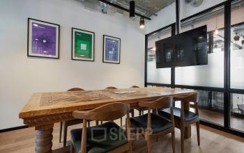 Moderner Konferenzraum zur Büroraum-Miete in der Friedrichstraße 68, Berlin Mitte. Raum mit Holztisch, Stühlen, Wandkunst, Glastrennwand und Bildschirm. Perfekt für Meetings und kreative Zusammenarbeit.