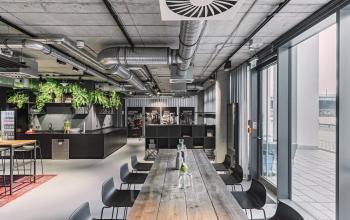 Modernes Büro im Alexanderufer 3-7, Berlin Mitte, mit industrieller Decke, langen Holztischen und Pflanzen, perfekt zum Büroraum mieten.