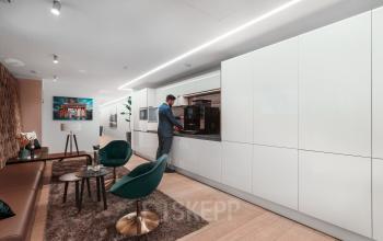 Schickes Büro mit modernen Möbeln und einer Person, die in der Küche Kaffee zubereitet. Option für Büro mieten im Berlin Mitte, Pariser Platz 6a.
