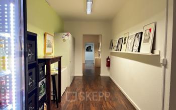 Blick auf einen schlichten Korridor im Bürogebäude An der Kolonnade 11, Berlin Mitte. Entlang der Wände sind Kunstwerke angeordnet, links steht ein Getränkeautomat. Ideal, um Bürofläche zu mieten.