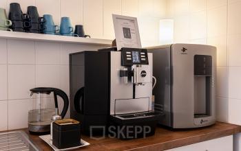 Küchenzeile in einem Bürogebäude mit Kaffeemaschine, Wasserkocher und Bechern auf Holzarbeitsplatte, ideal für Büroraum mieten in Berlin Mitte.