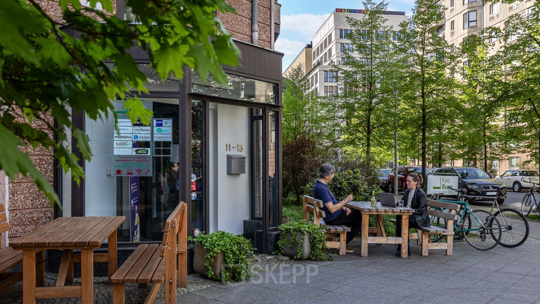 Zwei Personen sitzen draußen vor einem Gebäude in An der Kolonnade 11, Berlin Mitte, und arbeiten an Laptops. Perfekt für ein Büro mieten in einer lebhaften Umgebung.