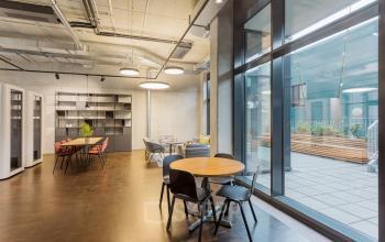 Modern office space with large windows, open floor plan, several round tables, and chairs at Hussitenstraße 32, Berlin Mitte.